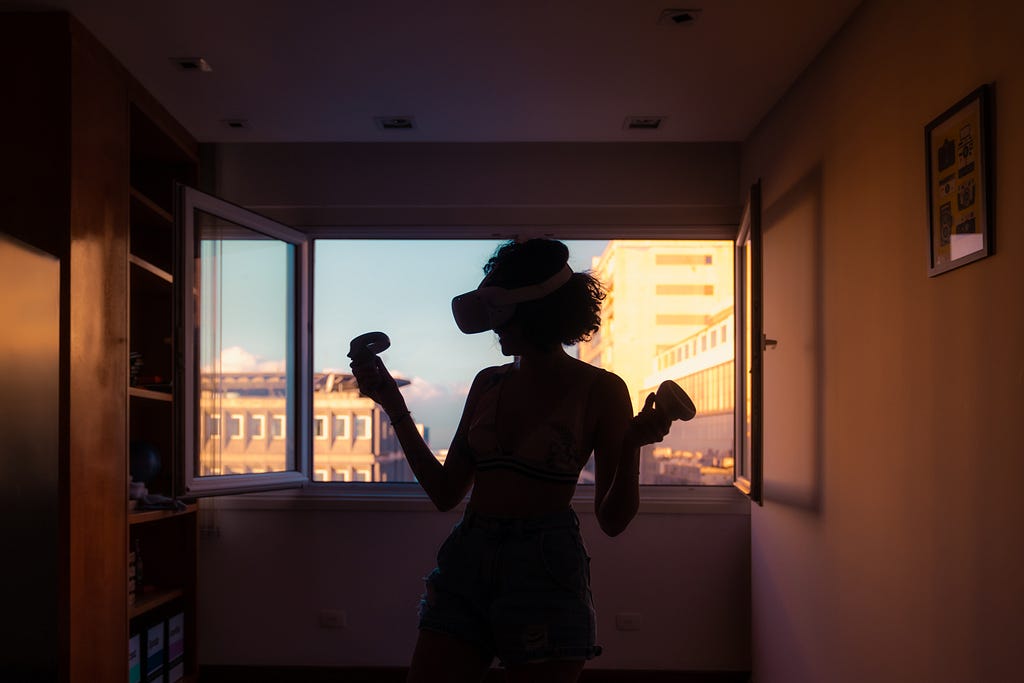 Woman with VR headset on and controllers in hands at sunset.