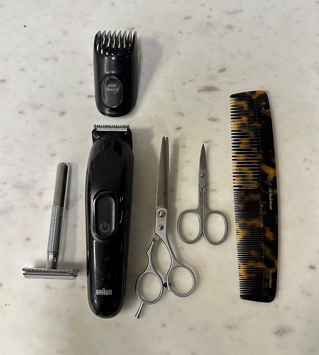 A safety razor, beard trimmer, attachment, large and small scissors and comb laid out.