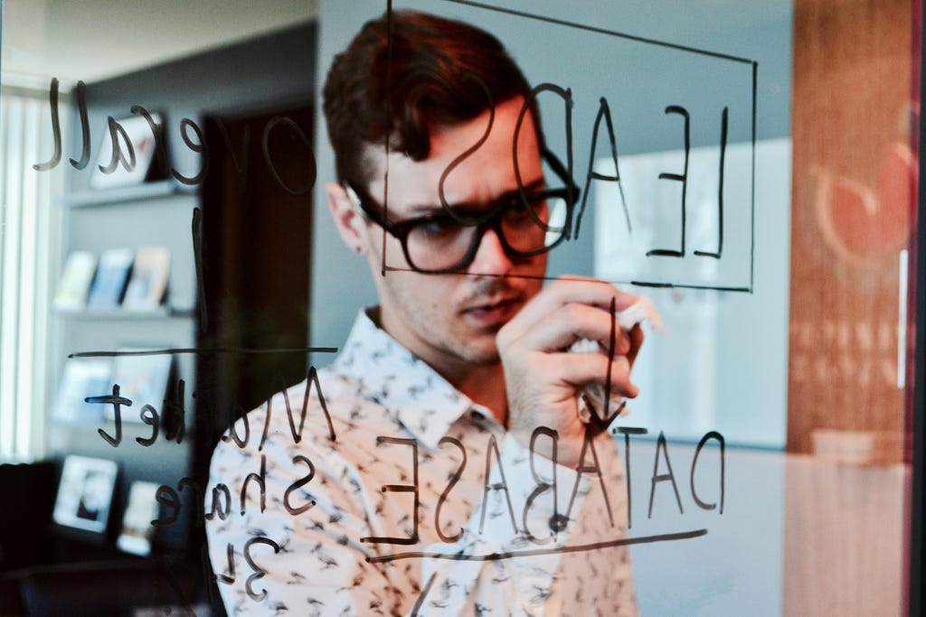 A man, seen through a glass surface, writing the word ‘leads’ with connections extending to other subjects.