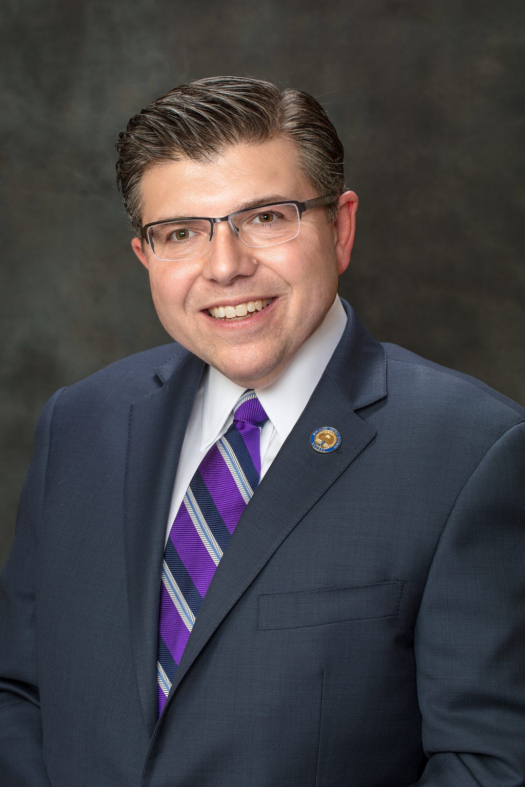 A head shot of New Jersey State Senator Tony Bucco. Bucco is wearing a gray suit and a purple, gray, and black necktie.