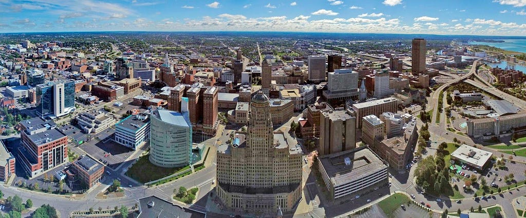 An aerial photograph of Buffalo, New York’s skyline filled with buildings, warehouses, roads, and coastal view.