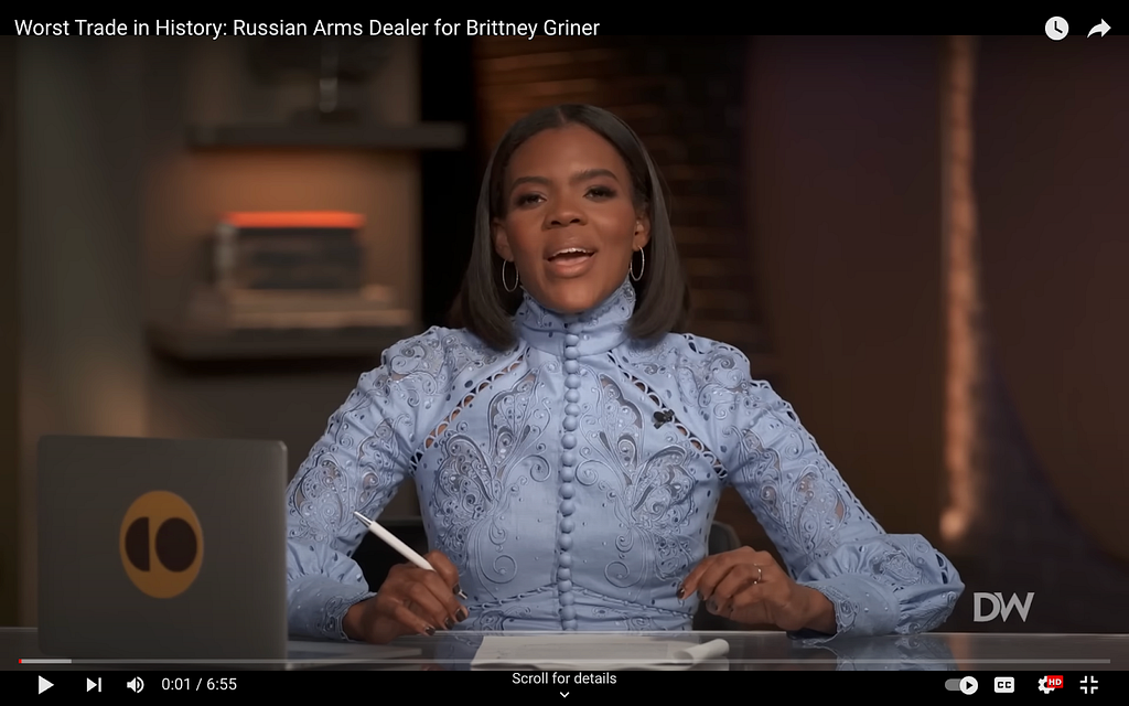 A screenshot from Candace Owens’s show on The Daily Wire. She wears a high collar, periwinkle blue dress with ornate designs. The dress has long sleeves and a line of buttons all the way up the front to the neck.