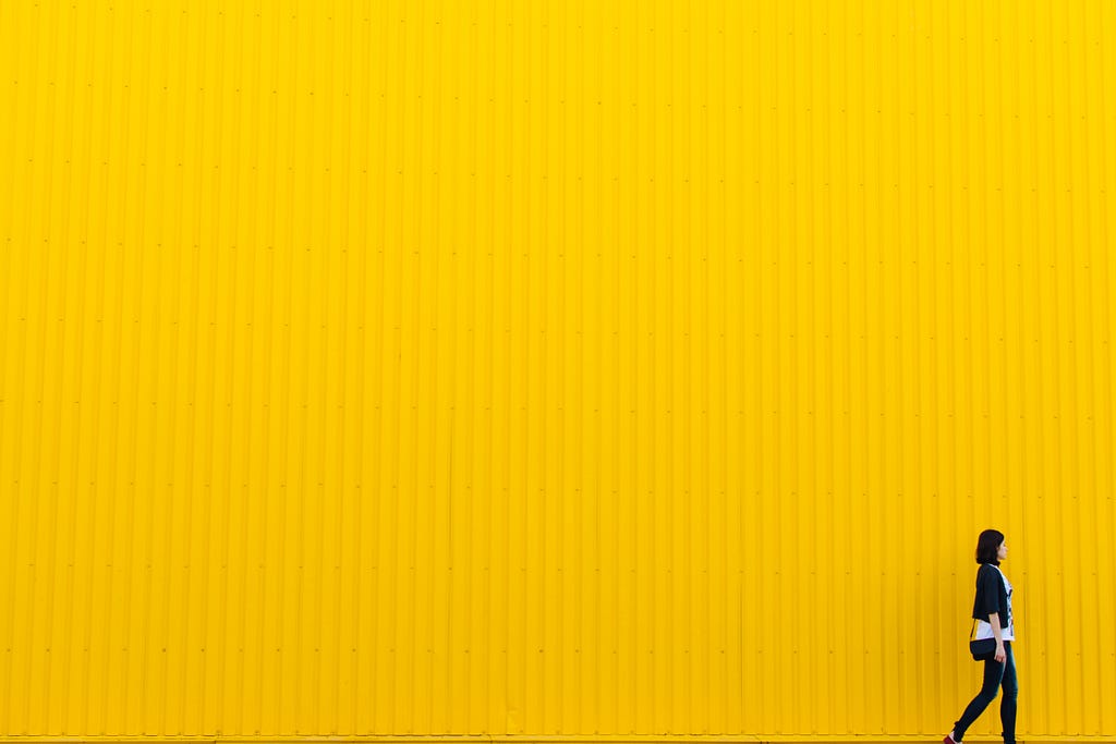 A woman walking with a yellow background (negative space)
