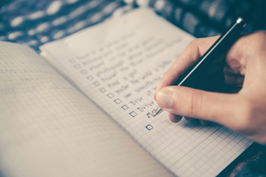 Photo of an open notebook with a list on it and a person’s hand checking items off the list.