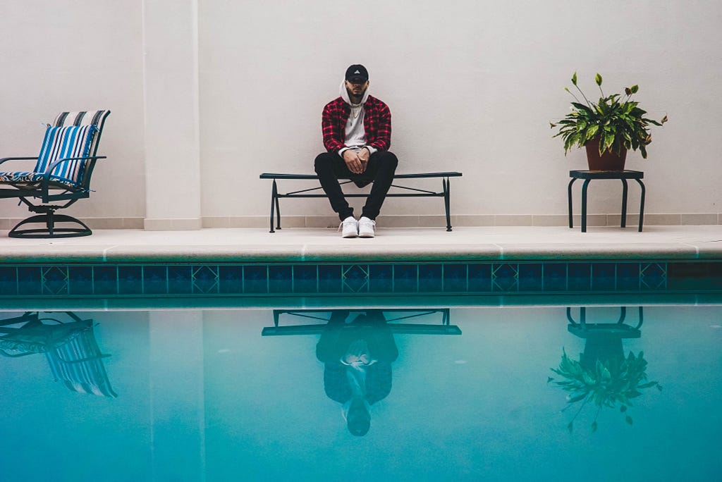 A man sits disappointingly beside a swimming pool.