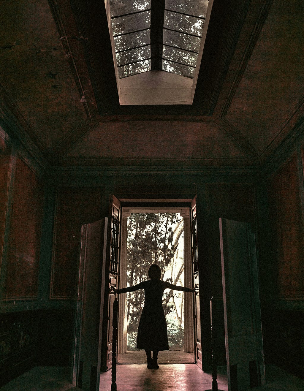 Picture of a lady standing at a door that seems dark on the inside but the outside is bright. Used to depict an imperfection that leads to new horizons.