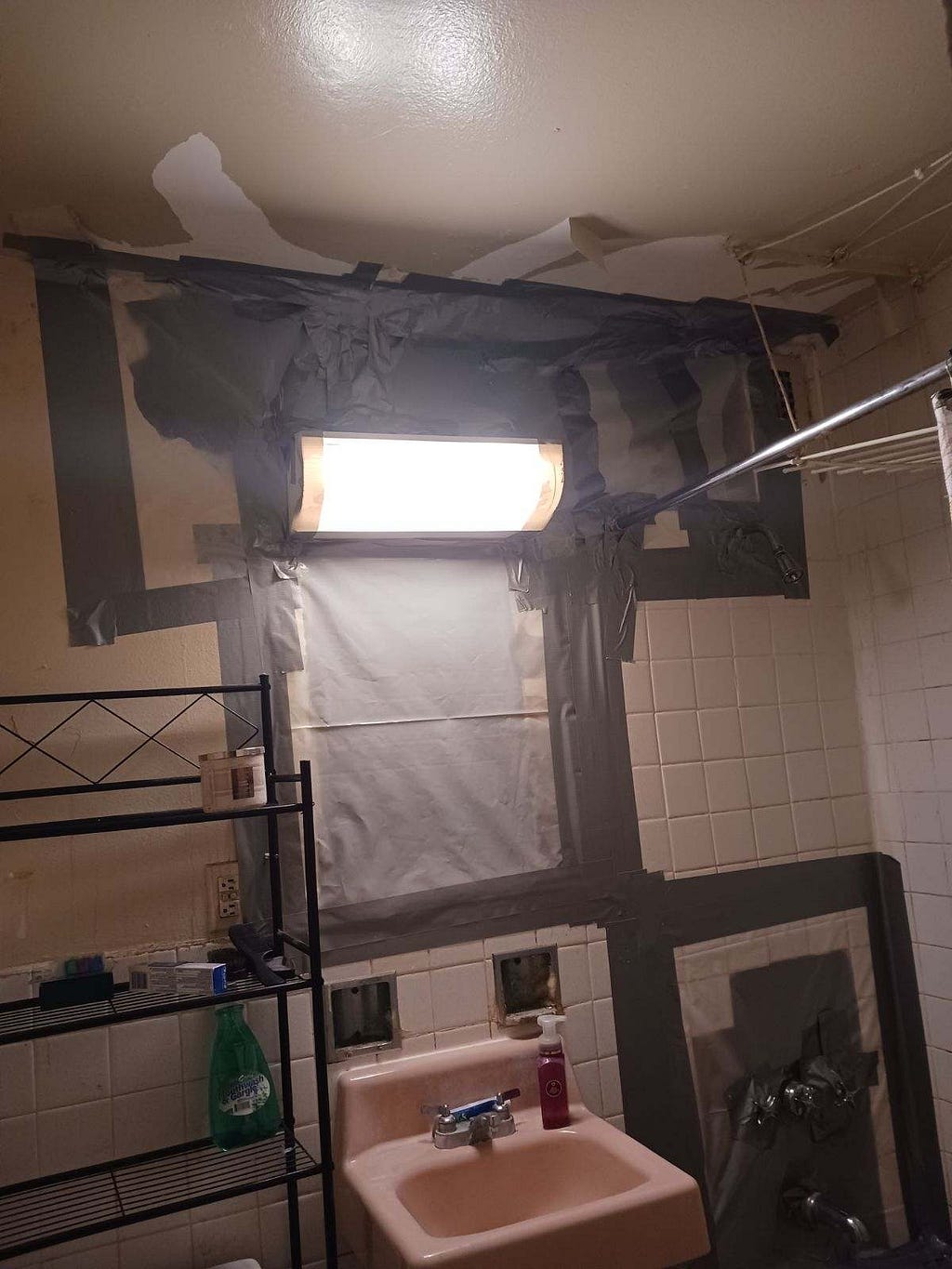 The wall of a bathroom covered in tape, indicating cutting through the wall done for repairs.