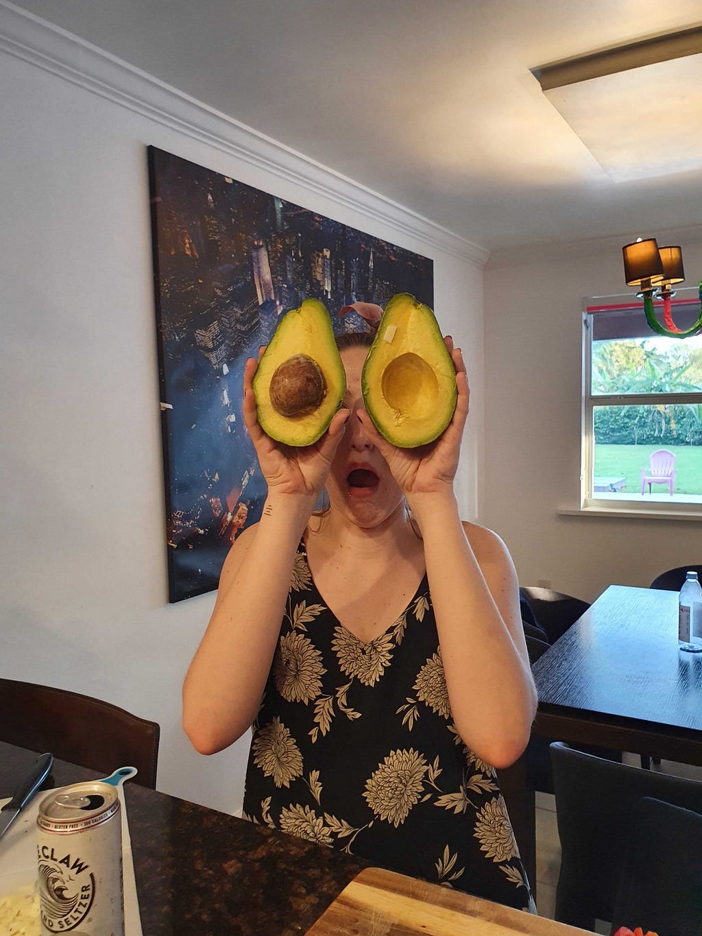 A woman holding up avocado halves in front of her eyes.