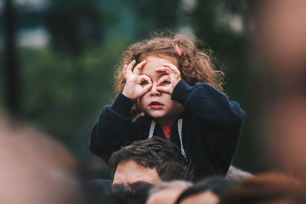 Cute photo of a child imitating glasses around her eyes with her hands on daddy’s back