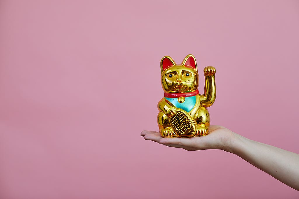 Golden lucky kitten (Maneki-neko) with pink background.