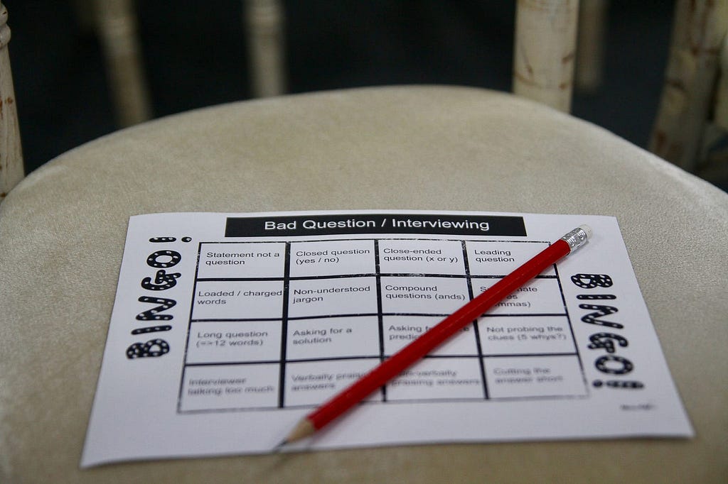 A paper bingo grid is shown placed on a chair with answers shown and a pencil placed on top of the paper.