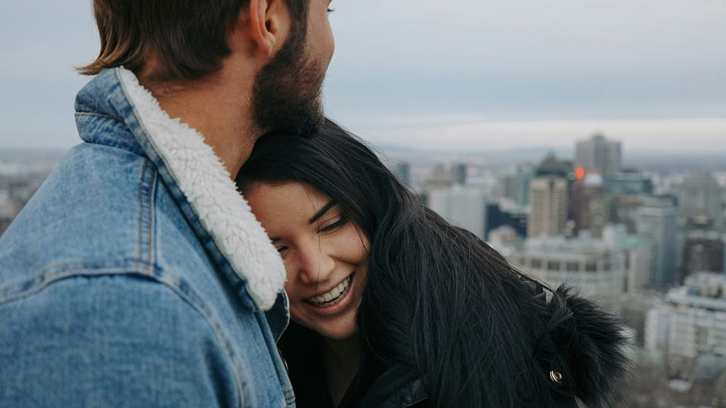 An image of a smiling girl resting her head on a guy’s chest.