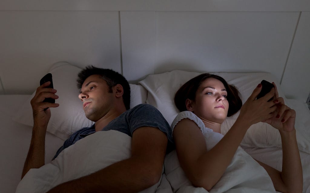 Young couple doomscrolling with their smartphones in their bed