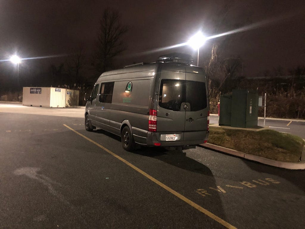 Camper van parked next to garbage dumpsters.