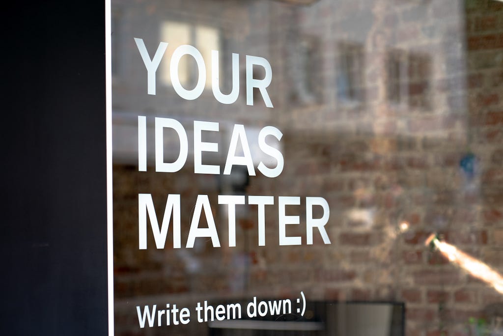The Statement, “YOUR IDEAS MATTER, Write them Down :)” written on the glass in front of a store