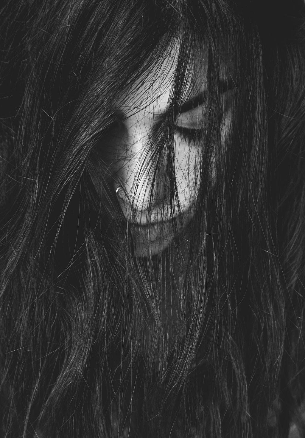 Sad woman with long dark hair covering her face.