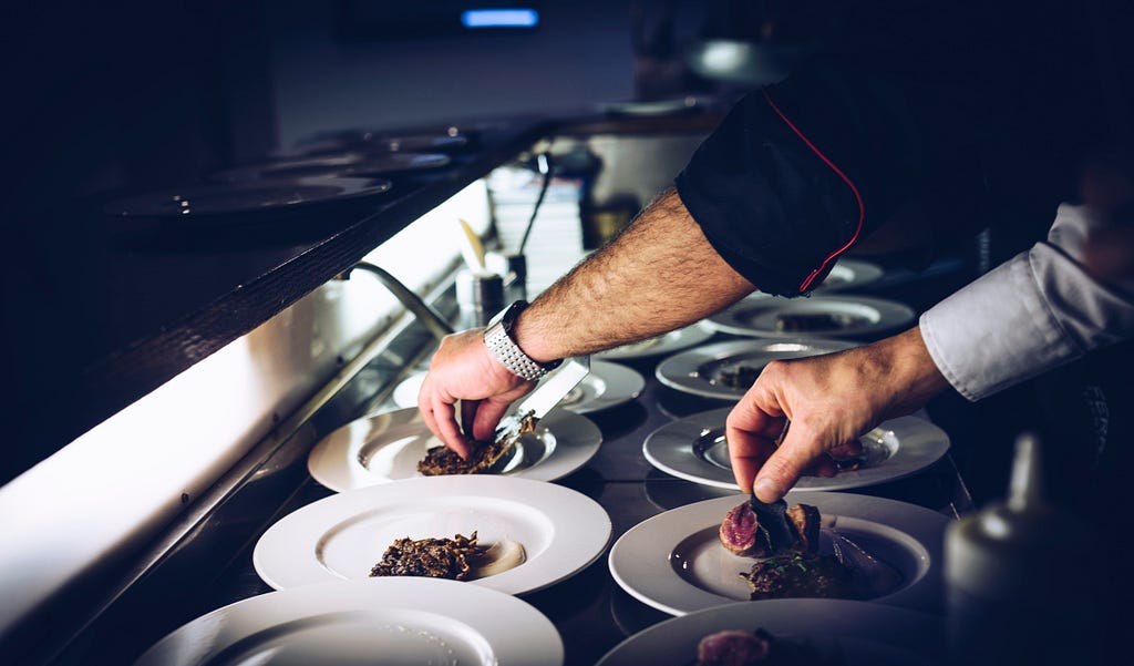 In a fine-dining kitchen, two chefs carefully arrange food onto plates