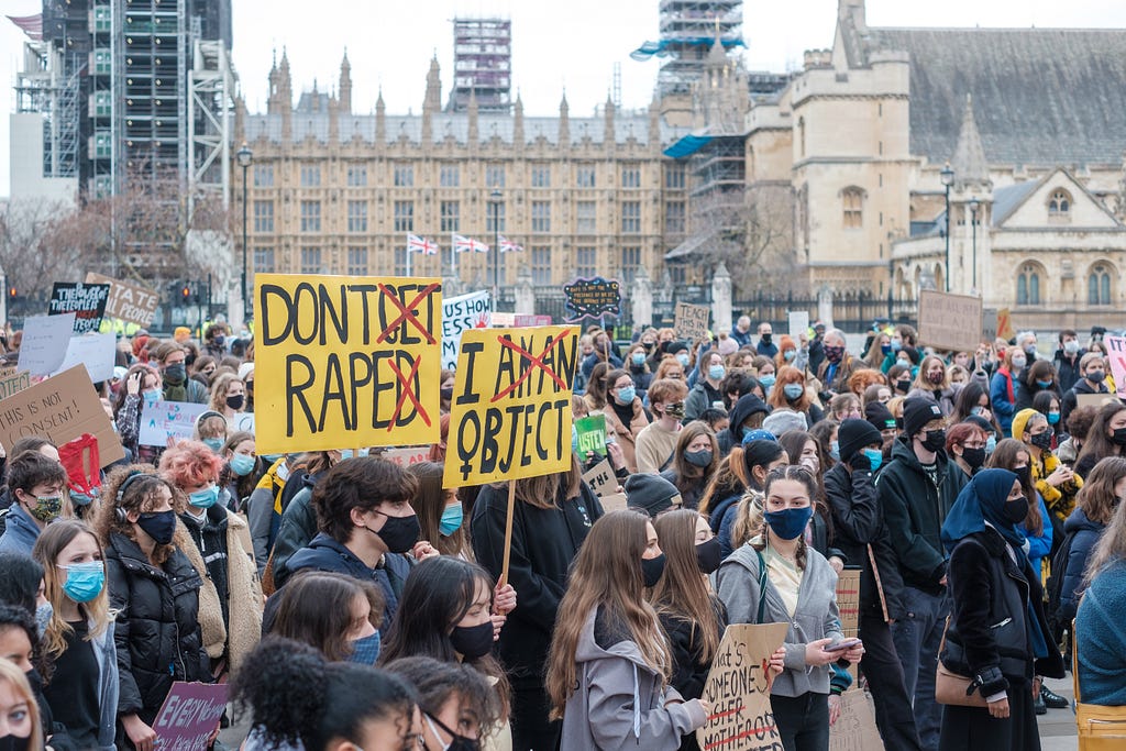 Group protesting with signs that say Don’t Rape (with Don’t Get Raped Crossed out) and I object with I am an object crossed out