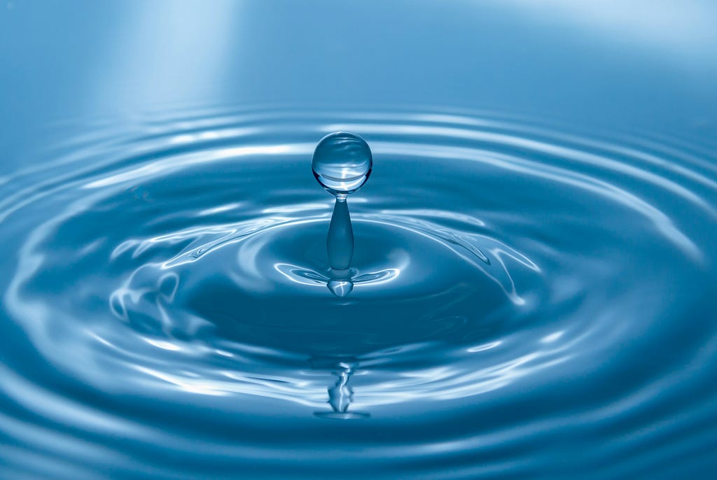 Blue droplet splashing back up after hitting a pool of water.