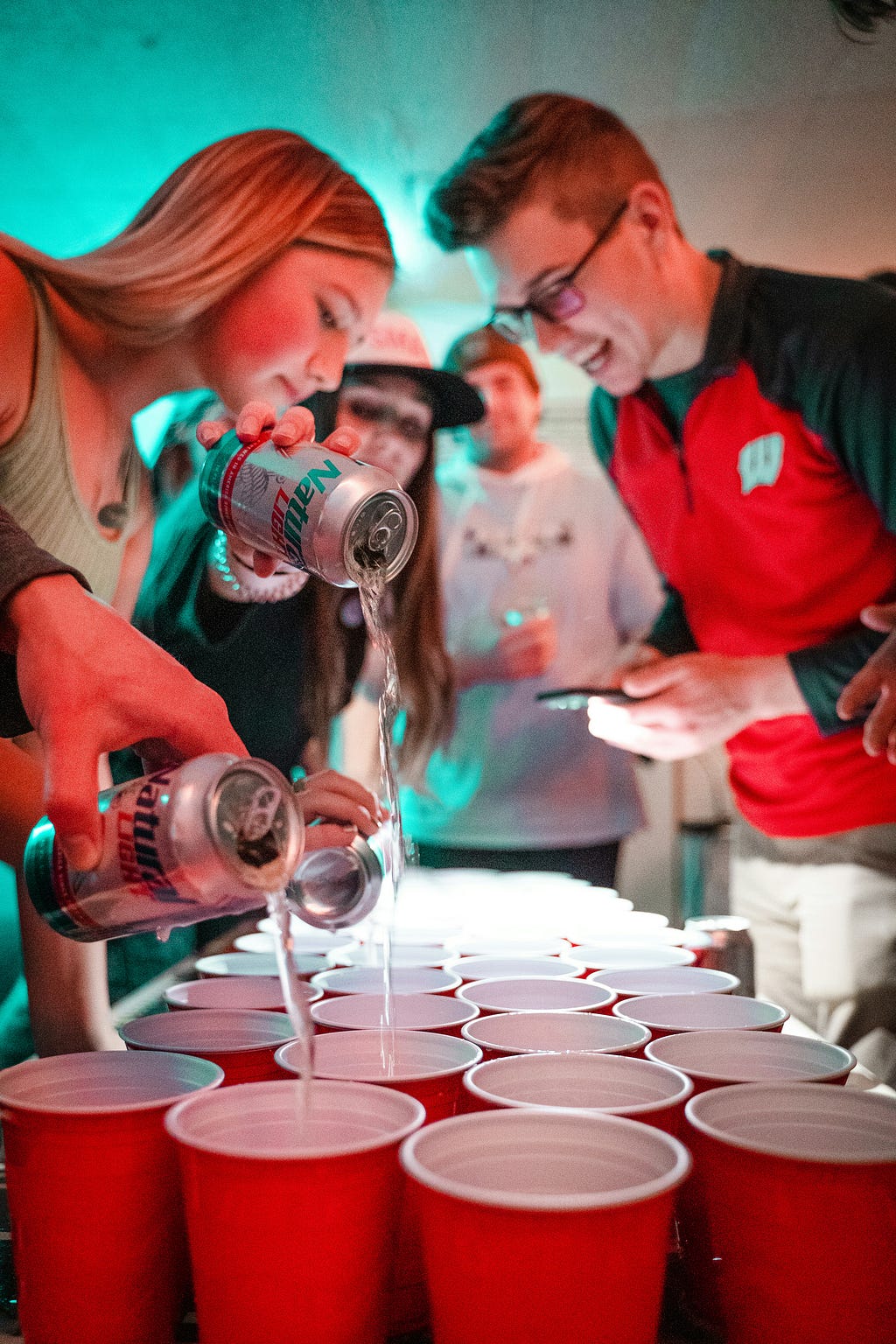 young people pour cheap beer into solo cups, preparing for a game of beer pong, aka Beirut