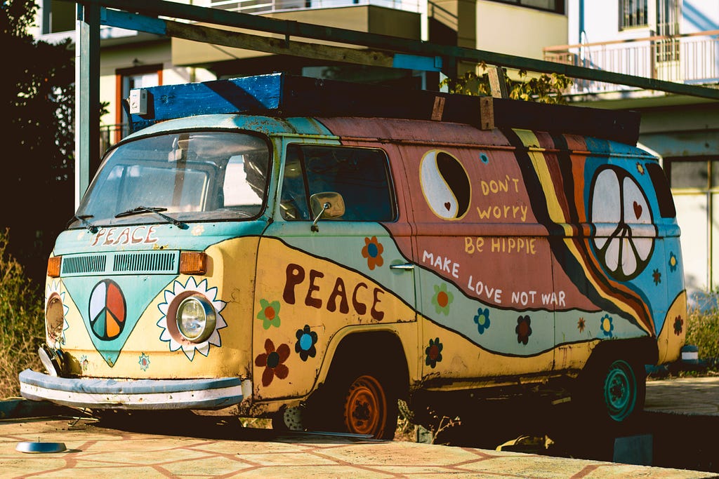A vibrant photograph of a colorful 1960s VW van decorated with the phrases “Peace”, “Don’t worry be hippie”, and “Make love not war”.