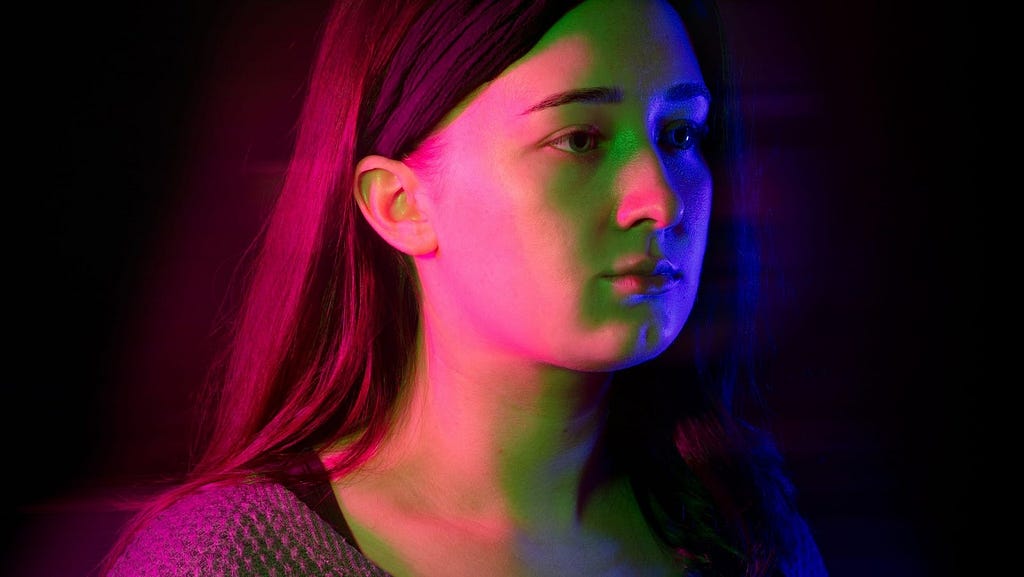 An image of a girl with red, blue and green lighting on her and a black background