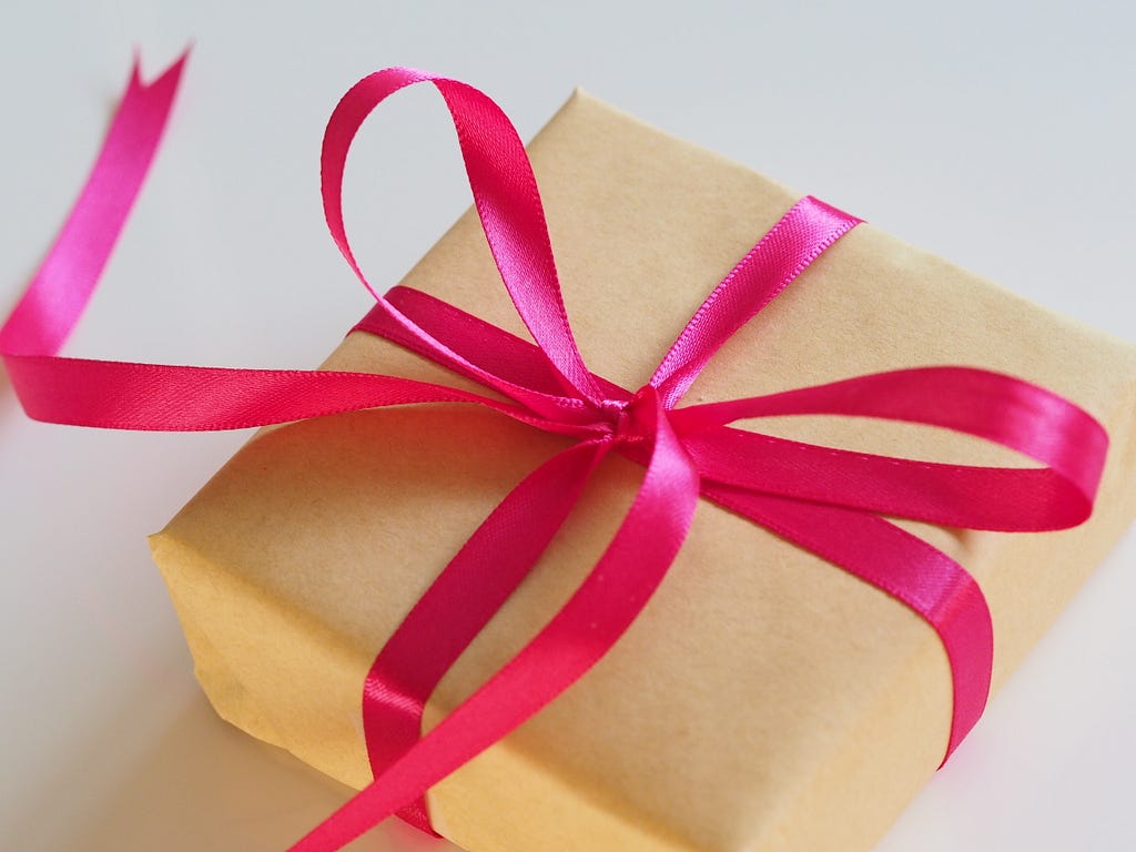 A gift box wrapped in brown paper and tied with a bright red ribbon