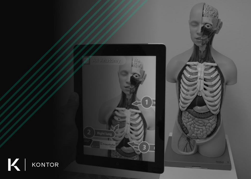 Person holding a tablet pointed at a medical training statue of a human with their internal organs expose. On the tablet, an augmented reality (AR) application is showing organ names in relation to the training statue. On the left side is the Kontor logo and a green Kontor watermark.