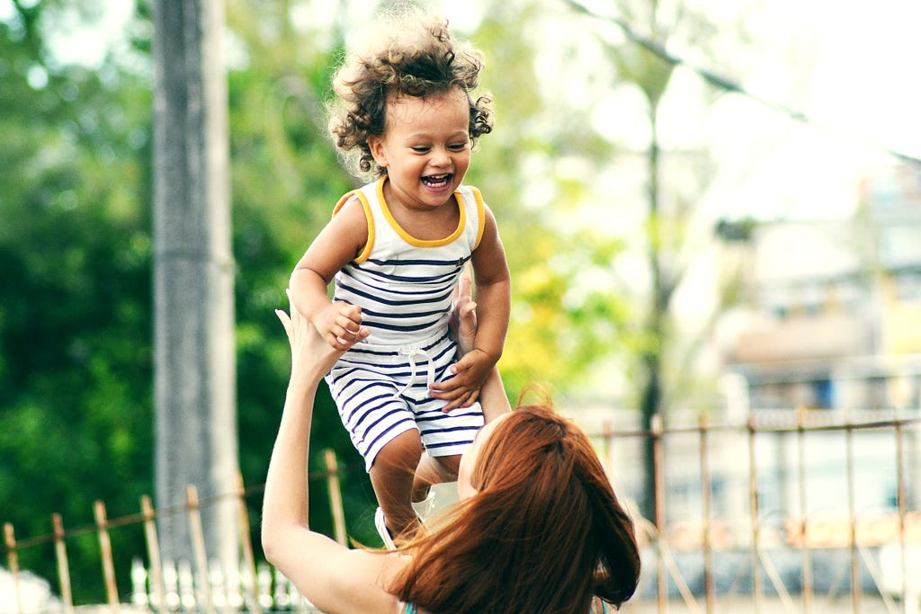 A mom tosses her child in the air. The child is smiling