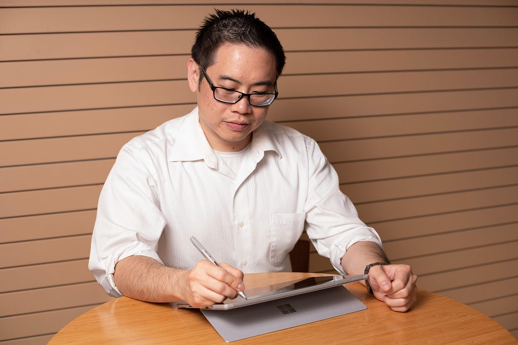 Steven Chan writing on a Microsoft Surface Pro computer.