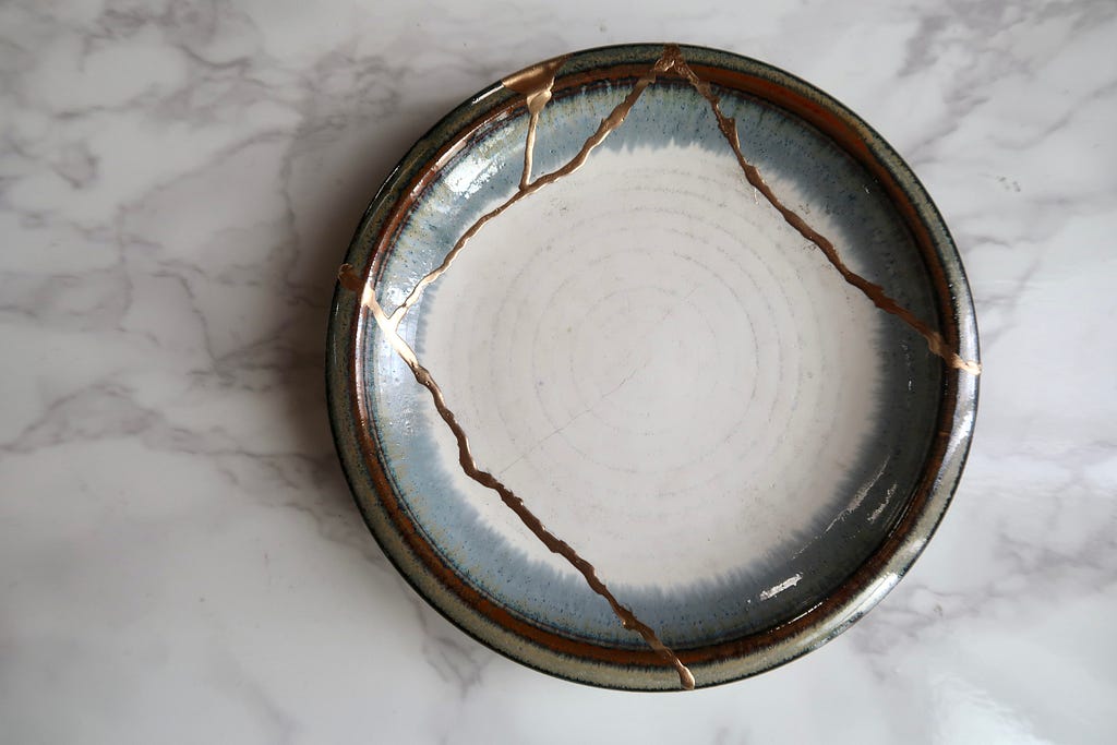 A white and grey bowl repaired together with gold streaks across the surface