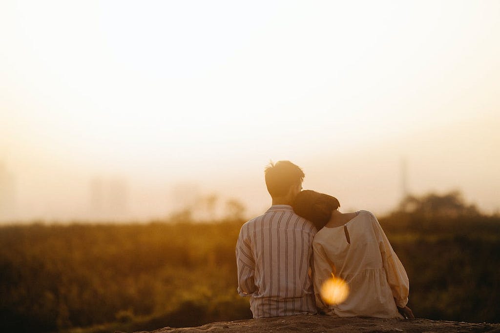 A couple sitting and looking at the sunset while the girl is leaning his shoulder
