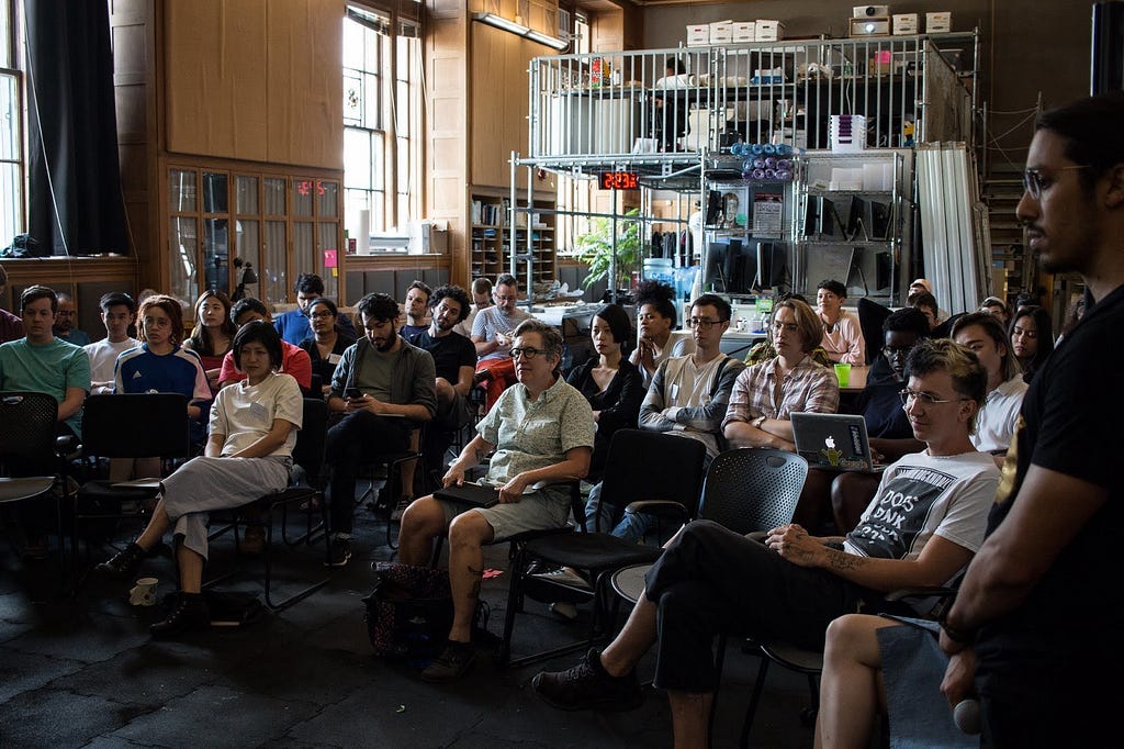 Descrição da imagem: Participantes assistem atentamente a uma apresentação na Conferência para Contribuidores p5.js.