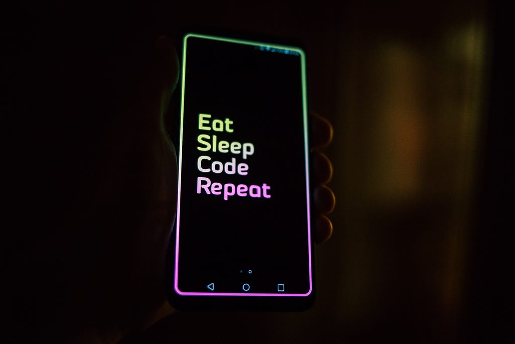 Mão segurando celular com os dizeres “Eat, Sleep, Code, Repeat”