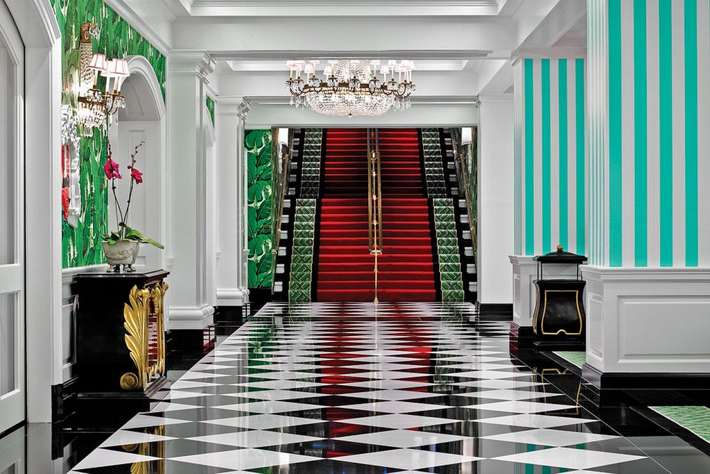 Hotel hallway with black and white checker floor, blue and white striped walls, flowers and chandelier.