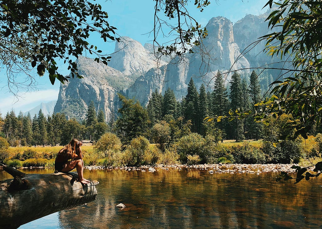 A person sits in front of a lake surrounded by mountains