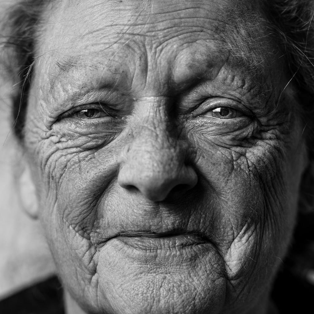 A black and white close-up photo of an elderly woman with a sudden but warm smile