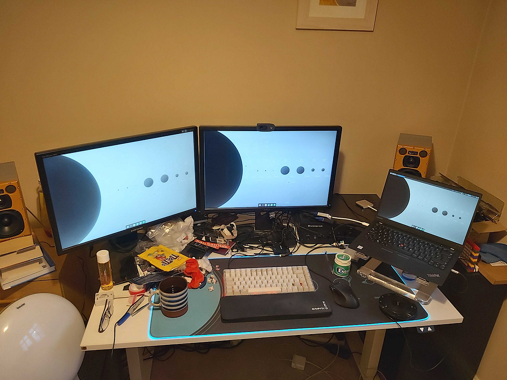 A picture of Mike’s desk, with a laptop on a stand, two monitors and a mechanical keyboard.