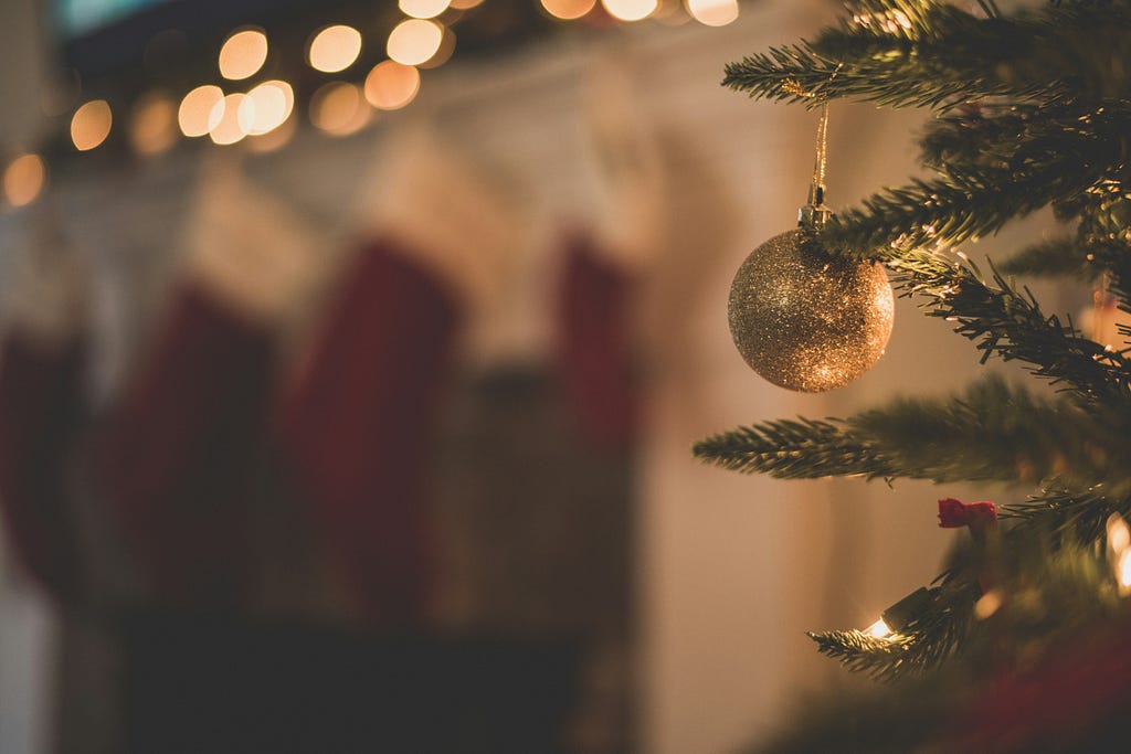 Blurred photo; stockings hang from a mantel in the background with a single gold ball ornament on a tree in the far right foreground.
