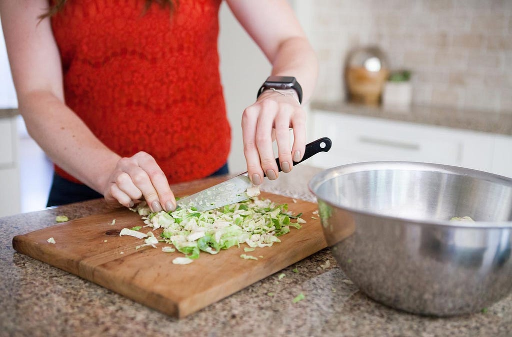 woman's hands holding knife chopping brussels sprouts on a wood cutting board