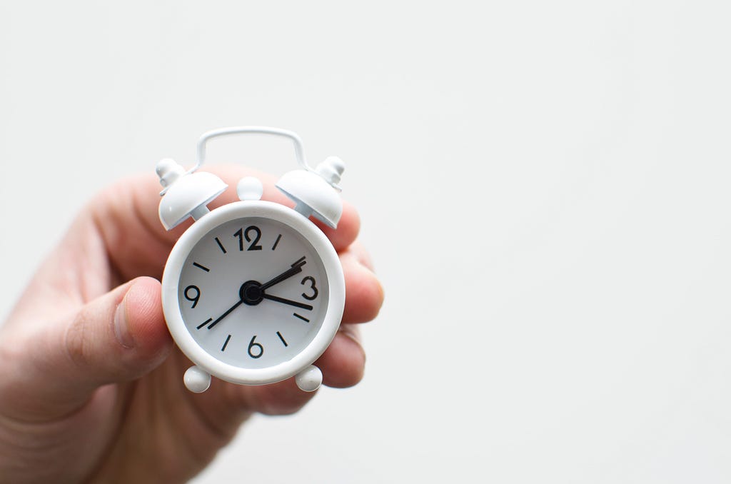 Hand holding a small white alarm clock.