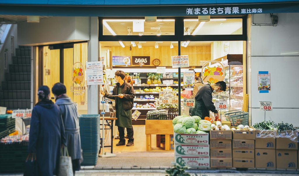 A couple of people standing and checking the goods in front of a Japanese store.