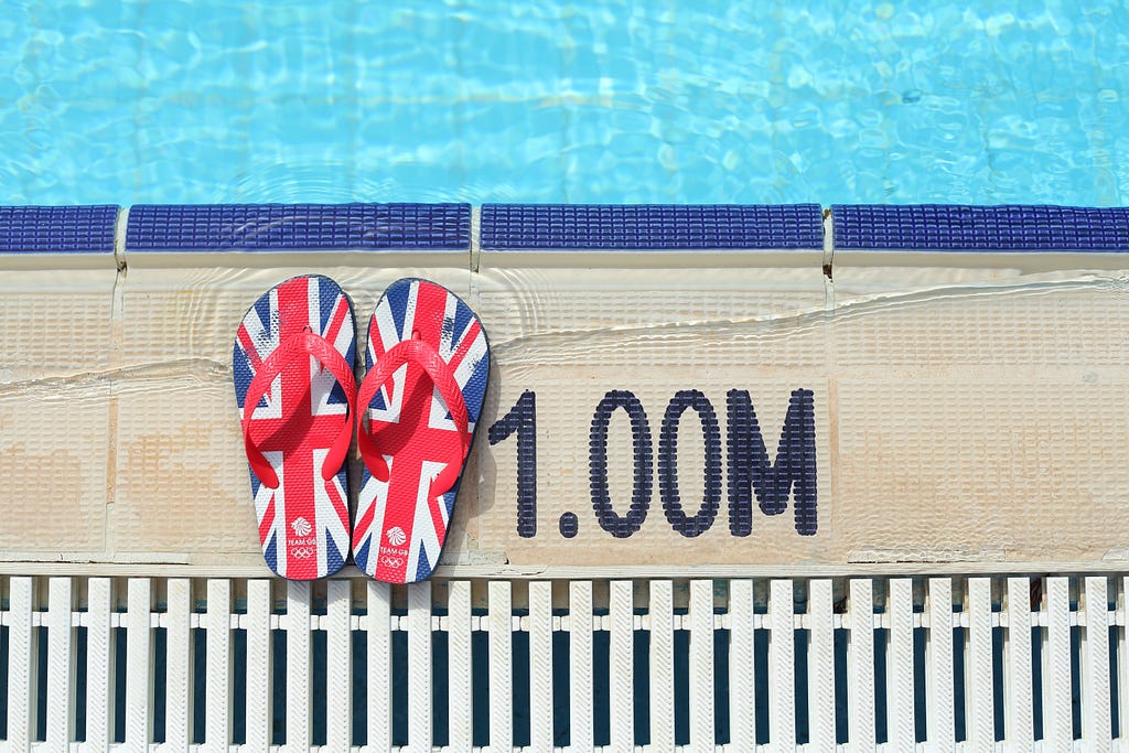 A pair of red, blue, and black Union Jack flip-flops sit by the pools edge.