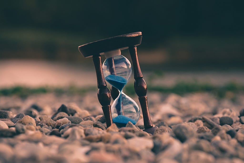 A sand timer containing blue coloured sand on gravel.