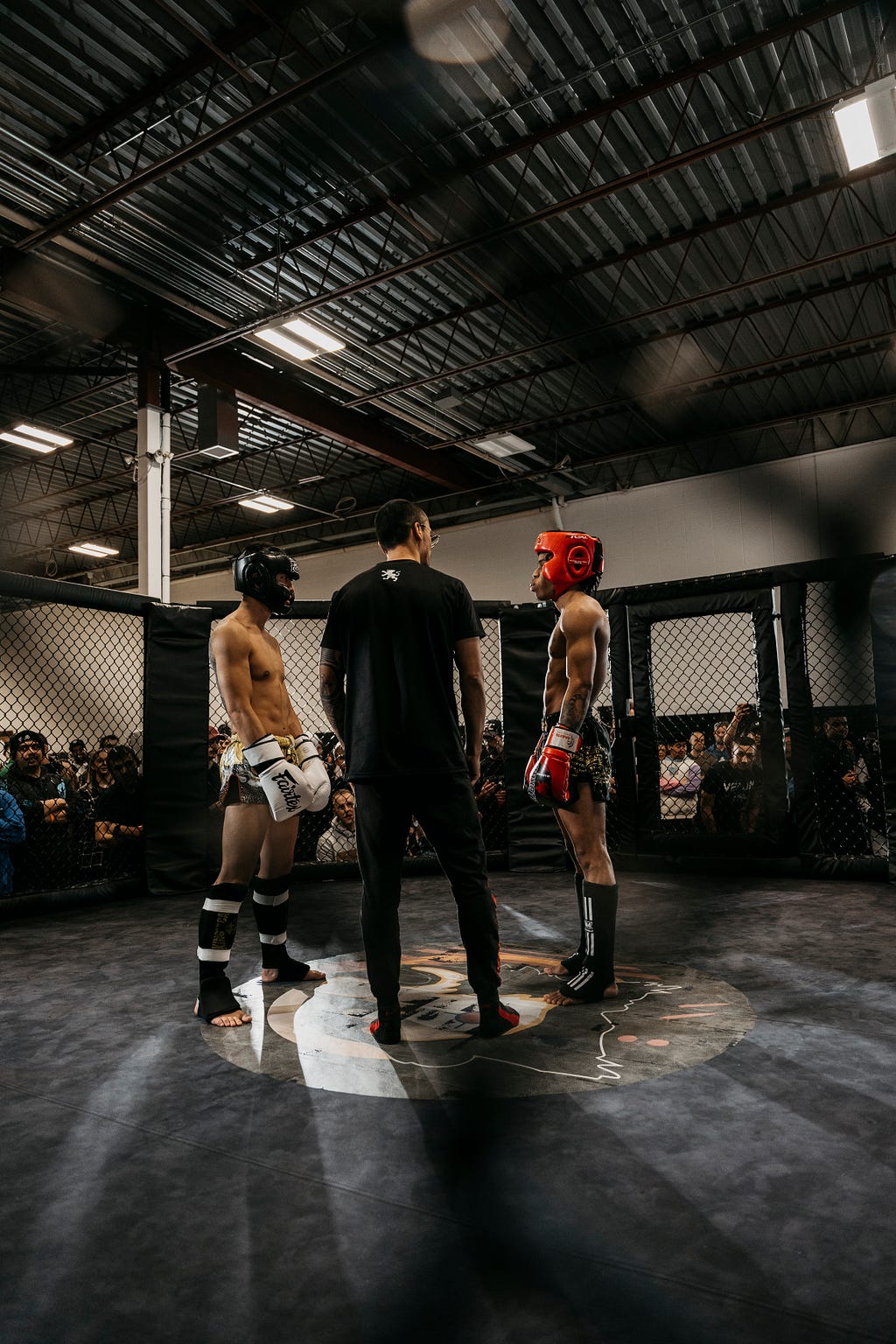 Two boxers calmly look at each other before a sparring session with the referee standing between them.