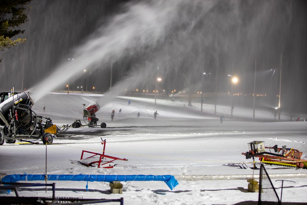 Machines blowing snow onto the slopes at night.