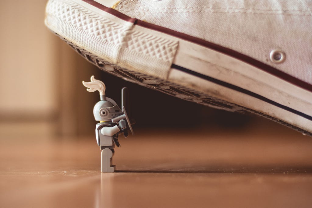 A tiny toy soldier holds a sword, above is the shoe of a human