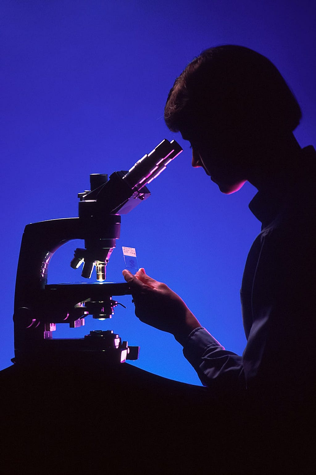 A woman (most likely a scientist) looking at a sample through the microscope