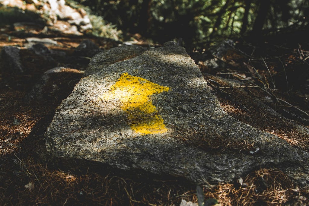 A rock with a weathered yellow arrow spray painted on it.