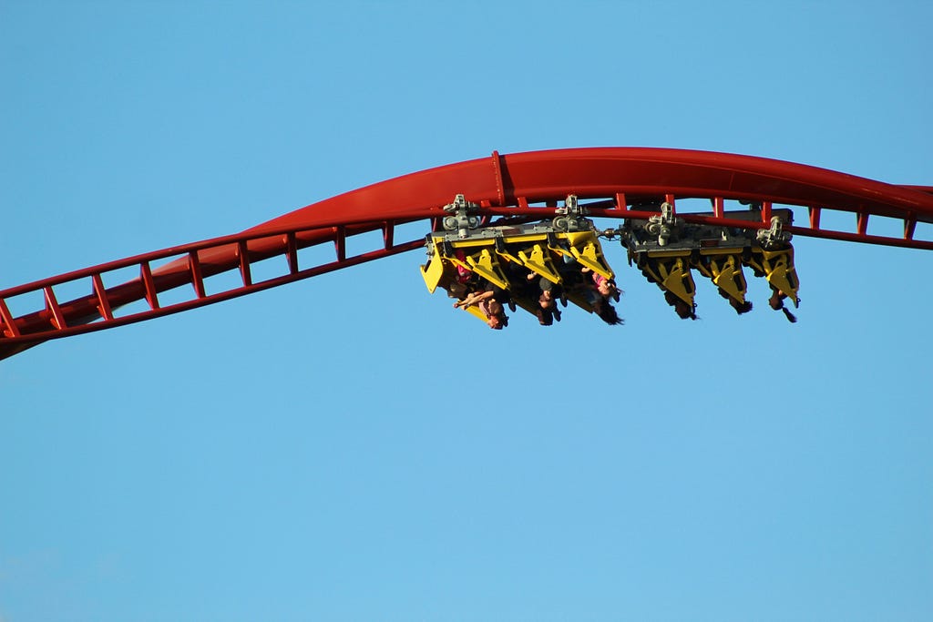 Two cars of a roller coaster upside down on red, twisting tracks.